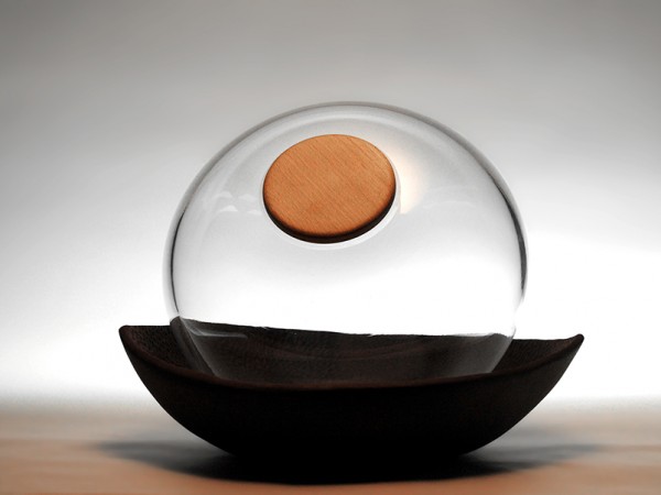 Urna furneraria para ceniza en vidrio soplado incoloro, cierre en madera y bandeja en barro negro esculpito.
